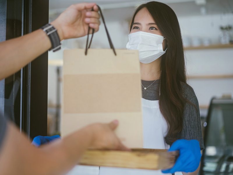 Waitress with face protective mask delivering takeaway coffee to customers.